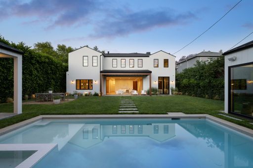 Modern white house with a swimming pool and lush garden at dusk, showcasing contemporary architecture and outdoor living space.