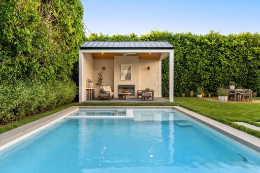 Modern backyard with a pool, patio, and lush greenery, featuring a stylish outdoor seating area under a covered structure.