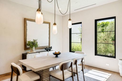 Modern dining room with minimalist decor, pendant lights, and large windows overlooking greenery.