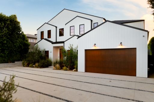 Modern white house with a wooden garage door and landscaped garden under a clear sky.