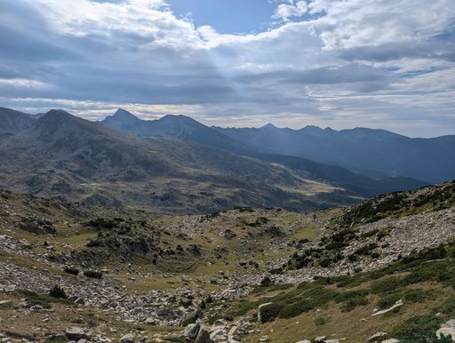 Panoramic view of rugged mountain landscape under a dramatic cloudy sky, showcasing the vast wilderness and natural beauty.