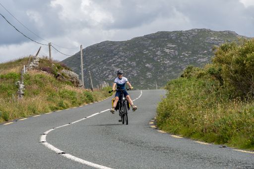 A young female cyclist smiling while riding her bicycle on the road in Connemara, Ireland