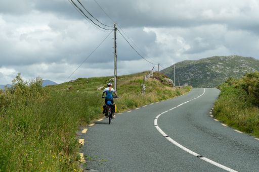 A cloudy morning at a road in Connemara, Ireland with a female cyclist riding her bik
