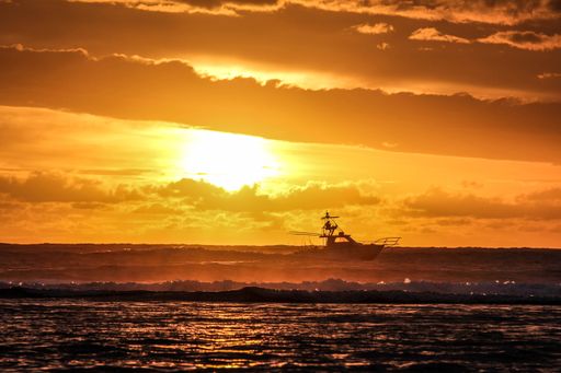 A beautiful shot of sea waves and a boat in the distance with the sun in the orange sky