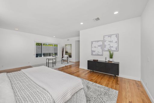 A modern bedroom interior with a cozy bed, wooden floor, and warm lighting
