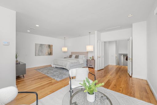 A modern bedroom interior with a cozy bed, wooden floor, and warm lighting