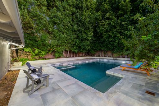 A modern backyard with a swimming pool, lounge chairs, and lush green trees