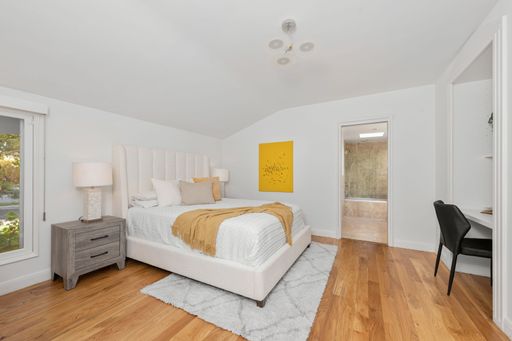 A modern bedroom interior with a cozy bed, wooden floor, and warm lighting