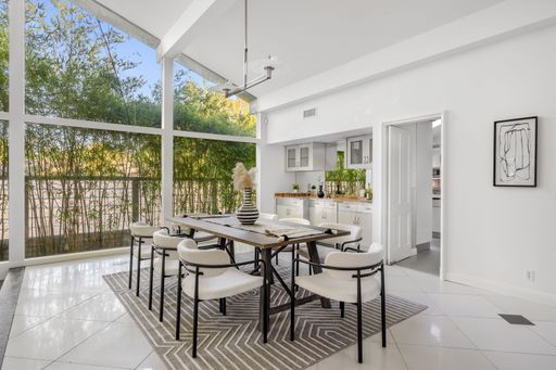 A modern dining room with elegant decor, featuring large windows and lush greenery