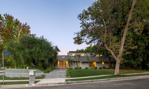 A modern residential home surrounded by lush trees and a well-maintained lawn