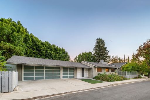 A modern suburban house with a spacious driveway, surrounded by lush greenery