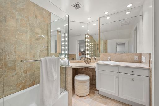 An elegant modern bathroom with marble tiles, large mirrors, and bright vanity lights