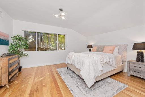 A modern bedroom interior with a cozy bed, wooden floor, and warm lighting