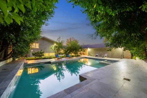 A modern backyard with a swimming pool, lounge chairs, and lush green trees