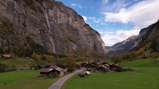Scenic view of Lauterbrunnen Valley with a waterfall cascading down a steep cliff, surrounded by lush greenery and quaint Swiss chalets.