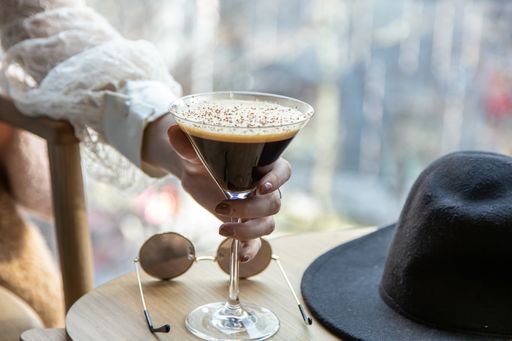 close up view of a woman's hand picking a martini glass filled with delicious chocolate coffee martini. sunglasses and black hat on coffee table