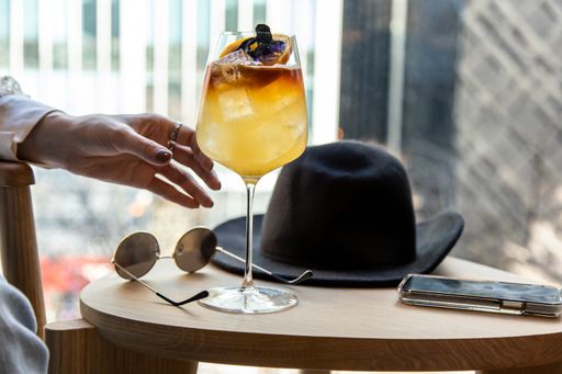 close up view of a woman's hand picking a wine glass filled with delicious natural herbal tea liquor sunglasses and black hat on coffee table
