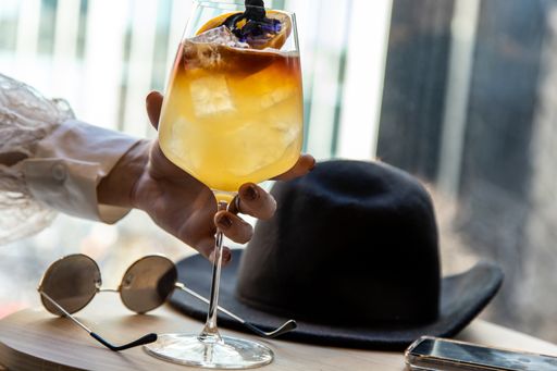 close up view of a woman's hand picking a wine glass filled with delicious natural herbal tea liquor sunglasses and black hat on coffee table