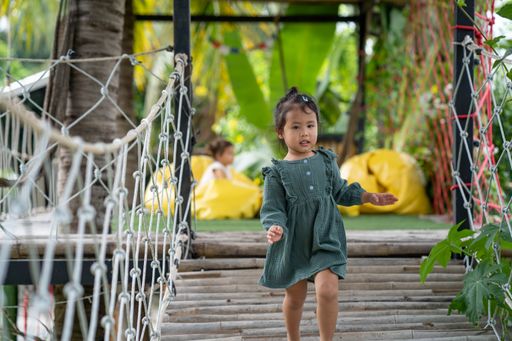 A little girl walking on the bamboo wooden bridge at the playground.