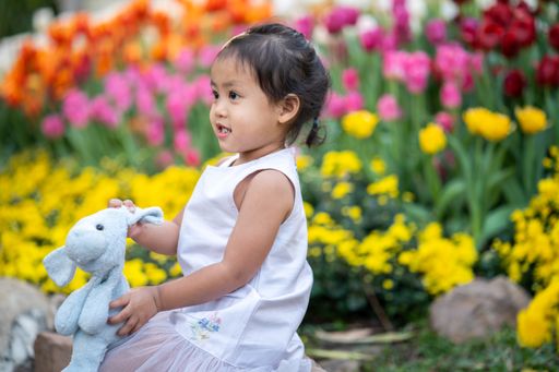 A cute little girl sitting in the flower garden holding a dog doll