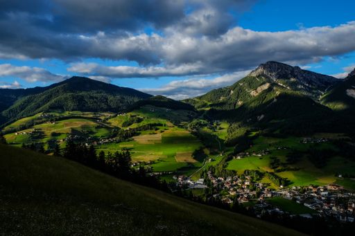 A beautiful shot of green hills and buildings near grassy fields with trees under a blue sky