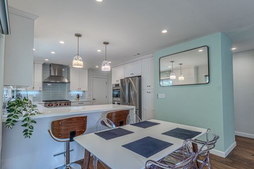 Modern kitchen interior with white cabinets, stainless steel appliances, and pendant lighting over a breakfast bar and dining table.