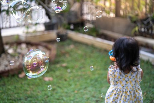 A closeup of a little girl blowing soap bubbles outdoors.