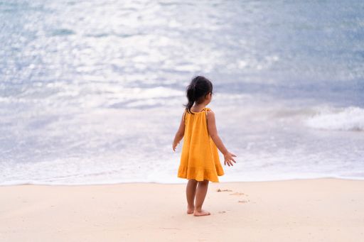 A cute Southeast Asian female child yellow dress standing at Kata Noi beach in Phuket Thailand