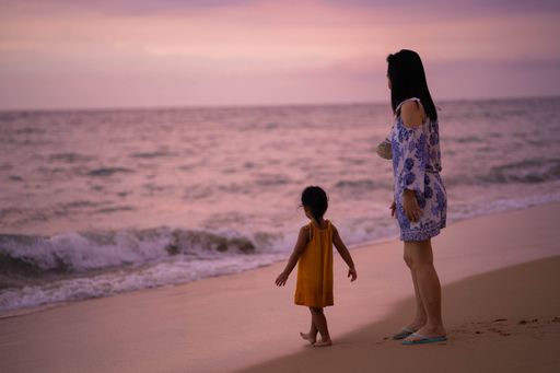 A shot of a woman and a cute little girl in a yellow dress on the beach during a beautiful sunset
