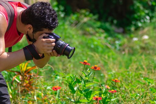 A closeup of a Hispanic man taking pictures of vibrant flowers while wearing a Covid mask