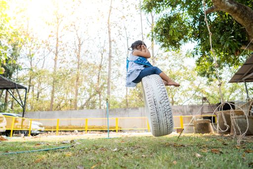 A little Thai girl hanging on a swinging car tires at a playground