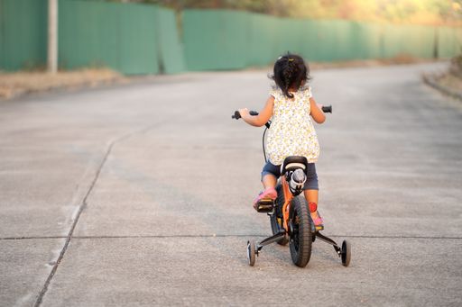 A back view of cute little Thai girl riding a bicycle in a park