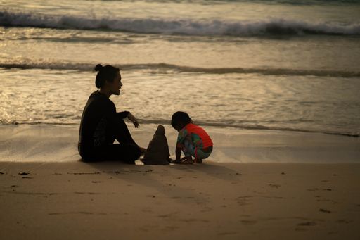 Beautiful silhouettes of mom and kid sitting on the seashore at the sunset