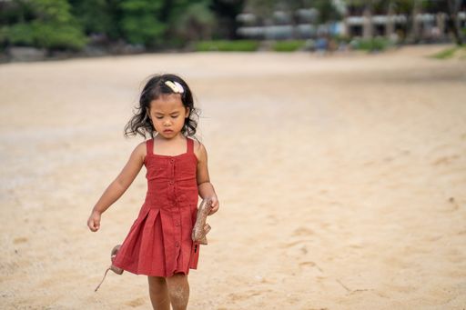 A beautiful southeast Asian female kid standing on the beach in a red dress in Thailand