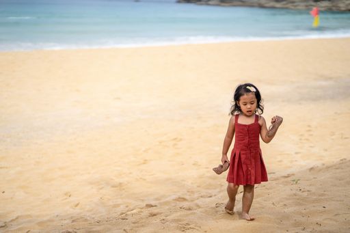 A beautiful southeast Asian female kid standing on the beach in a  red dress in Thailand