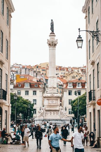 People walking near the Rossio Square in Lisbon with the Pedro IV Column in the background on a cloudy day.