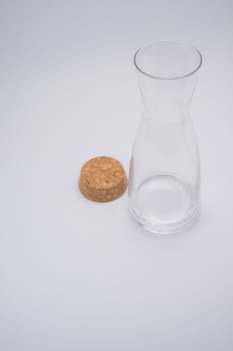 A vertical shot of a clear glass bottle with cork stopper isolated on a gray background