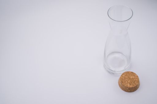 A high angle shot of a clear glass bottle with cork stopper isolated on a gray background