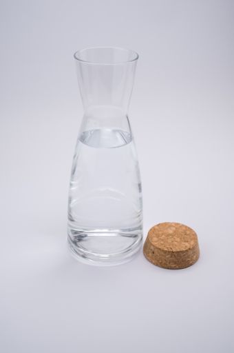 A vertical shot of a clear glass bottle with cork stopper isolated on a gray background
