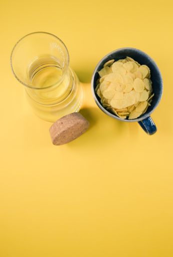 A clear glass bottle with cork stopper and cup of corn flakes isolated on a yellow background