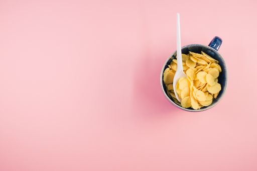 A top view of corn flakes on a cup with plastic spoon isolated on a pink background