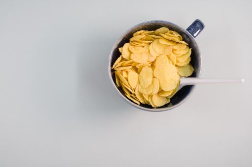 A top view of corn flakes on a cup with plastic spoon isolated on a light gray background