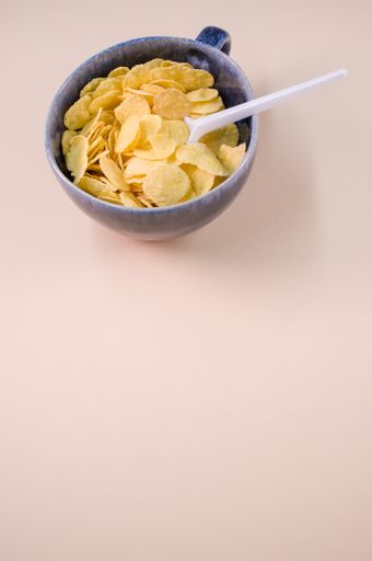 A vertical shot of corn flakes on a cup with plastic spoon isolated on brown background