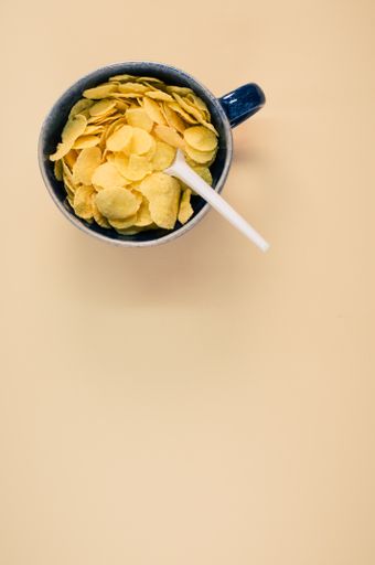 A vertical shot of corn flakes on a cup with plastic spoon isolated on brown background