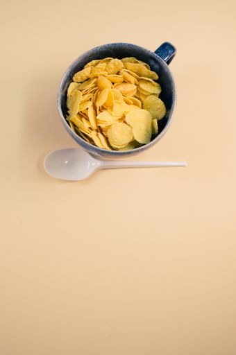 A vertical shot of corn flakes on a cup with plastic spoon isolated on brown background