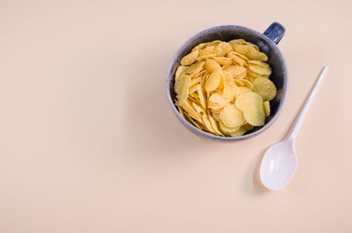 A top view of corn flakes on a cup with plastic spoon isolated on brown background