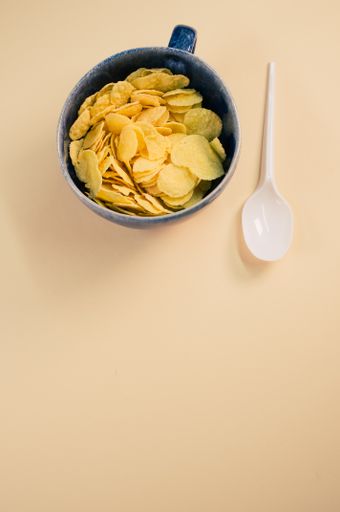 A vertical shot of corn flakes on a cup with plastic spoon isolated on brown background