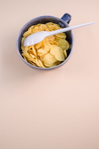 A vertical shot of corn flakes on a cup with plastic spoon isolated on brown background
