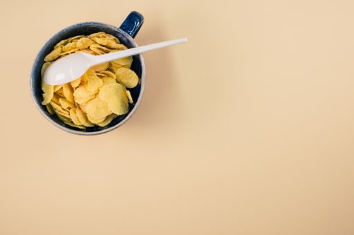 A top view of corn flakes on a cup with plastic spoon isolated on brown background