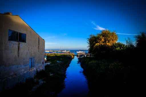 A lake in the middle of the grassy field and a house near the sea with blue sky in the background